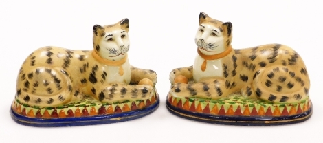 A pair of Staffordshire style seated cats, each cat with ball on a green stepped base on blue circular surround, unmarked, 15cm high, 23cm wide.