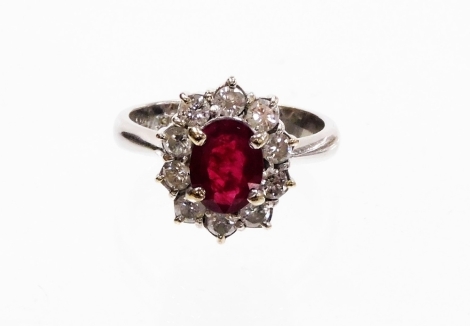 A ruby and diamond dress ring, with oval cut central ruby, 7.8mm x 6mm x 2.4mm, in a four claw setting surrounded by round brilliant cut tiny diamonds, each approx 0.05cts, on a raised ring head, white metal stamped 750, ring size M, 5.5g all in.