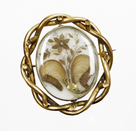 A Victorian memorial brooch, with central oval panel with locks of hair and flower type design, in a rolled gold mount, on single pin back, 5cm x 4cm.