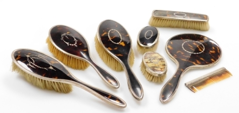 A George V silver and tortoiseshell backed dressing table set, comprising three hand brushes, hand mirror, small brush, a cream tortoiseshell brush, long handled brush and a comb. (AF)