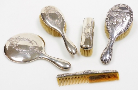 An Edwardian silver backed dressing table set, comprising mirror, hand brush, long brush and a comb, all in similar design with neoclassical type bow detailing, Birmingham 1910, together with a later silver backed brush with berry design, Chester 1906. (5