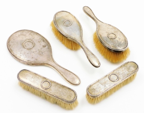 A George V silver backed dressing table set, comprising two hand brushes, two long brushes and a hand mirror, each with ribbed design and central applied circle cross detailing, London 1918. (5)