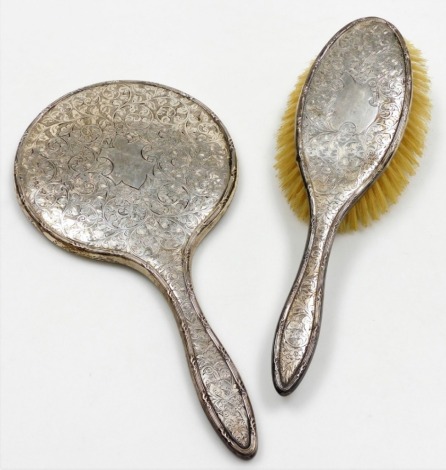 A George V silver backed heart dressing table set, comprising hand brush and mirror, each with embossed floral scroll decoration, Birmingham 1916. (2)