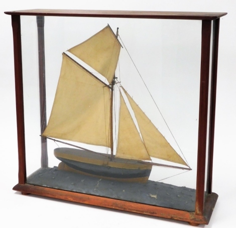 A glazed model yacht, the wooden yacht with four masks and painted in brown and black, mounted in a display case, 65cm high, 70cm wide, 22cm deep. (AF)