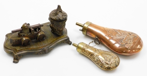 Two brass powder flasks and an inkstand, one brass pad flask with The Royal Fusiliers emblem, together with a floral rococo scroll detailing, together with a military tank inkstand, (AF), 9cm high and 17cm wide. (3)