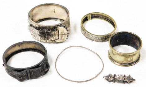 A group of silver and other bangles, to include a Victorian silver hanged bangle with buckle decoration and flowers, a silver plated napkin ring, two other hinged bangles one with buckle design, a white metal thin bangle unmarked and a silver bar brooch. 