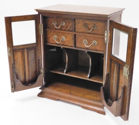 A 1920s oak smoker's cabinet, with two partially glazed doors opening to reveal four fitted drawers and shelved interior, on splayed feet, 44cm high, 37cm wide, 21cm deep.