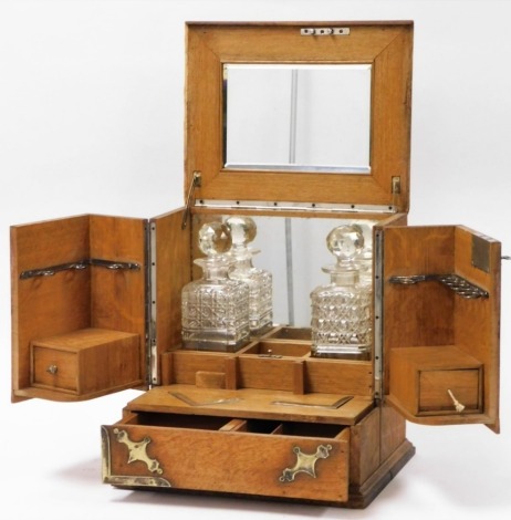 An early 20thC oak decanter stand, the outer case with brass inlaid shields opening to reveal mirrored top and back, with two decanters and boxed section, 36cm high, 35cm wide, 29cm deep.