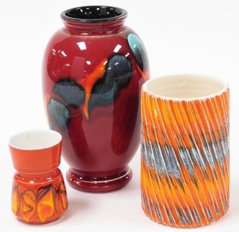 Three Poole pottery vases, to include a red Delphisware vase, 22cm high, an orange flared vase, 15cm high, and a red flambe vase, 10cm high. (3)