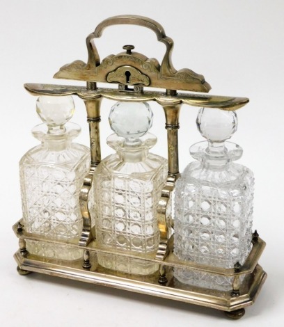 A late 19thC silver plated tantalus, with three cut glass decanters, in a raised key lock silver plated frame, heavily in scrolled, 38cm high, 32cm wide, 12cm deep.