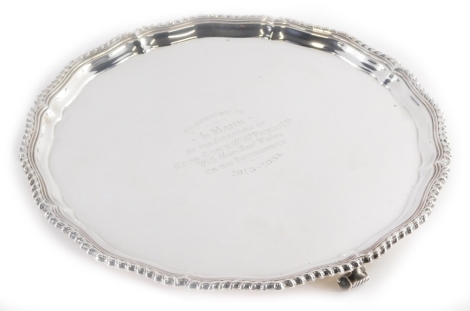 A George V silver salver, with a shaped and gadrooned border, the centre with the inscription 'Presented to L. Mann by the Directors of Cook Son and Co. (St Paul's) Ltd with Their Best Wishes on His Retirement 1913-1938', on three scroll feet, Birmingham 