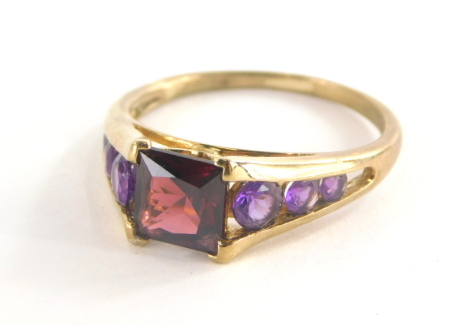 A 9ct gold dress ring, with square set red faceted stone and amethyst set tension shoulders, the band marked QVC, the central stone possibly garnet, ring size T, 3.3g all in.