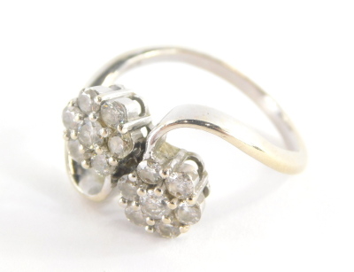 An 18ct white gold diamond twist ring, with two floral cluster diamond sections, on twist detailing, each diamond approx 0.10cts, in a claw setting, marked 750, ring size O½, 5.g all in.