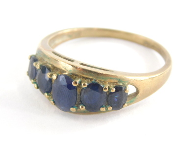 A dress ring, set with five oval cut dark blue faceted stones, pierced and oval setting on a yellow metal band stamped 9ct QVC, 3.3g all in. (AF)