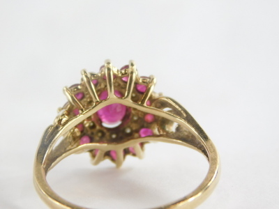 A 9ct gold cluster ring, with oval cut ruby in claw setting surrounded by cz stones and outer round brilliant cut rubies, on a two row twist design shoulders, ring size P½, marked QVC, 4.1g all in. - 2