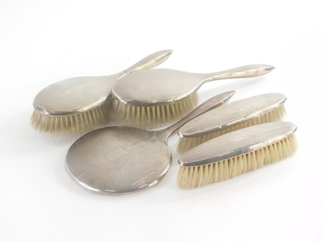A George VI silver mounted brush set, to include two hairbrushes, two clothes brushes and a hand mirror, with engine turned decoration and a vacant cartouche, Birmingham 1951.