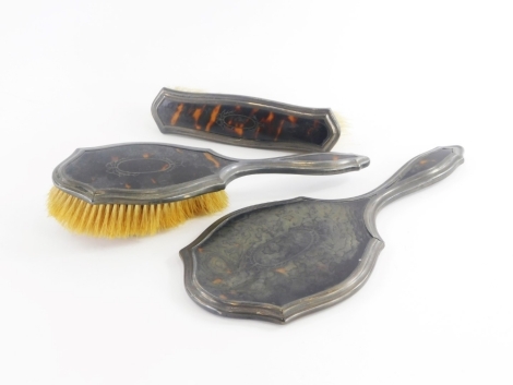 A George V tortoiseshell and silver mounted three piece dressing table set, comprising hand mirror, hairbrush and a clothes brush, Birmingham 1920 and 1923. (3)