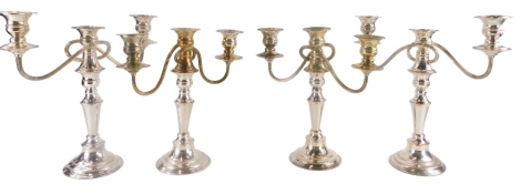 A set of four silver plated three branch candelabra, each with waisted stem and beaded borders, 30cm high, 30cm wide.