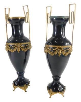 A pair of 19thC continental black glass two handled urns, with shaped brass handles, and a moulded brass band decorated with fruit, leaves and bows, on brass detachable feet, 39cm high. (2)