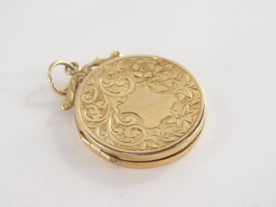 A circular locket pendant, marked with scroll pendant mounted top, and leaf design detailing, yellow metal unmarked, 2cm wide, 4.3g all in. - 2