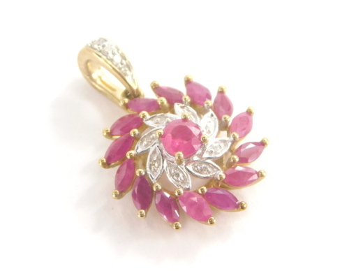 A 9ct gold ruby and diamond floral pendant, with central wave design flower on two rows bordering with central rubies, surrounded by diamonds and a halo of further diamonds, with diamond set pendant loop, 2cm high on a pierced open work back, 2.3g all in.