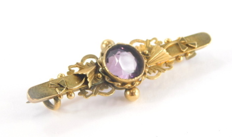 A Victorian bar brooch, with central round brilliant cut amethyst in a rub over and twist design setting, with scroll and floral detailing on yellow metal bar marked 9ct, 4cm wide, 2.4g all in.