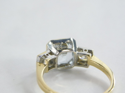 An aquamarine and diamond set dress ring, the square cut aquamarine in a rub over gold setting, with two round brilliant cut diamond shoulders each approx. 0.15ct, in platinum on a yellow metal band unmarked, believed to be 18ct, ring size N½, 3.7g all in - 2