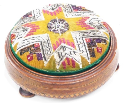 A Victorian walnut and parquetry footstool, with a bead work seat on bun feet, 27cm diameter.