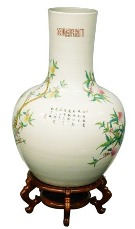 A large Chinese bottle shaped porcelain vase, decorated with peaches, blossom and script, 69cm high, and a hardwood stand.