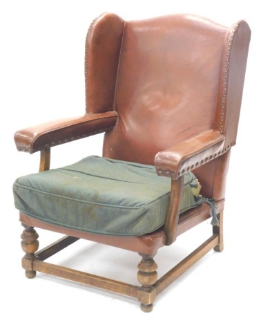 An early 20thC oak wingback chair, upholstered in brown leatherette on turned supports.