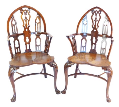 A pair of gothic style yew and elm Windsor chairs, by Gostin of Liverpool, each with a carved arched back, solid saddle seat, raised on cabriole legs, on pad feet, 110cm high, 53cm wide, 49cm deep.