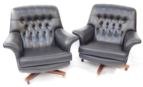 A pair of G-Plan mid century black leather swivel chairs, each on a wooden base with castors, with button back and detailing, 85cm high, 92cm wide, 85cm deep.