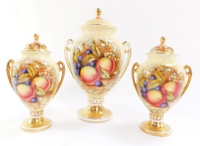 An Aynsley porcelain garniture of vases, each of twin handled, baluster form, with covers, decorated with fruit by D Jones, printed marks, larger vase 20cm high, pair of smaller vases, 14.5cm high. (3)