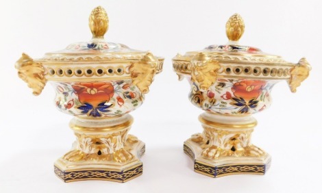 A pair of early 19thC Derby porcelain pot pourri vases and cover, of circular form, the lids with pineapple finials, bodies moulded with masks, raised on lion's paw feet and quatrefoil bases, imari decorated with panels of flowers, painted marks, 15cm hig