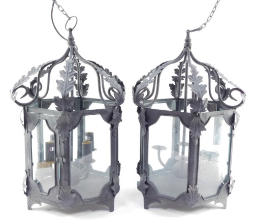 Two wrought iron hanging lanterns, each hexagonal with four branch central candle stand, with acanthus leaf detailing, on hanging loop, converted to electricity, 56cm high. (2)