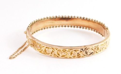 A 9ct gold hinged bangle, with two part floral detailing and half hinged outer filigree bordering, with safety chain, 6.5cm wide, 8.9g all in.