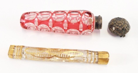 A Victorian cranberry flashed glass scent bottle, with a white metal mount and hinged lid, embossed with flowers, 11cm wide, together with a Georgian gilt decorated faceted glass scent bottle, 10.5cm wide. (2)