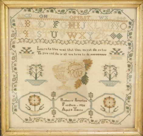 A George IV sampler by Rebecca Layton, Fordham, 1826, aged eight years, stitched with an alphabet, vase of flowers, trees in pots, and a verse Learn to Live Well... and Die is All We Have To Do, 25cm high, 26.5cm wide.