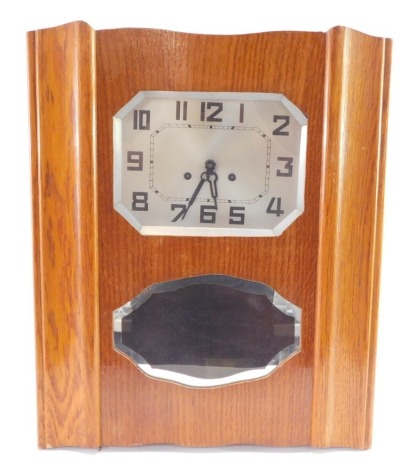 A continental mid century light oak cased wall clock, the octagonal silvered dial bearing Arabic numerals, eight day movement with rod strike, the case of shaped rectangular form, with inset bevel glass panel below the face, with pendulum and key, 54cm hi