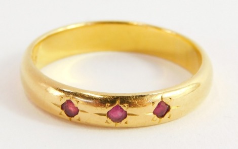 A 22ct gold wedding band, set with three rubies, size U, 6.2g.