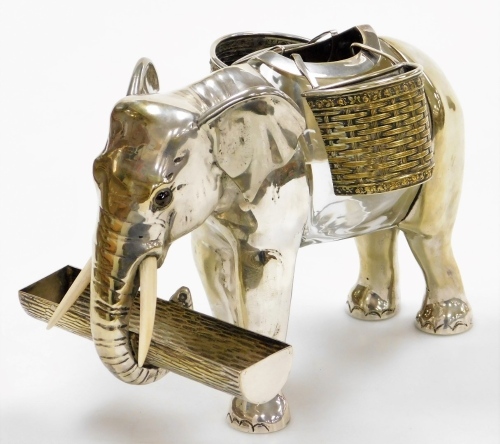 An early 20thC silver plated and glass centrepiece or posy holder, in the form of an elephant, with ivory tusks and glass eyes, the trunk holding a rectangular cylindrical vacant log shaped vessel, with a central vacant glass body with a removable section