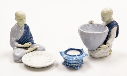 Three Lladro porcelain ornaments, comprising a Lladro figure of a seated monk with bowl, 14cm high, a figure of a kneeling monk carrying bowl, 15cm high, and a candle stand, 4cm high. (3)