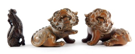 A pair of Chinese 19thC wooden carvings of dogs of fo, 8.5cm wide, and a Japanese carved wooden netsuke of a seated kirin, 7cm high.