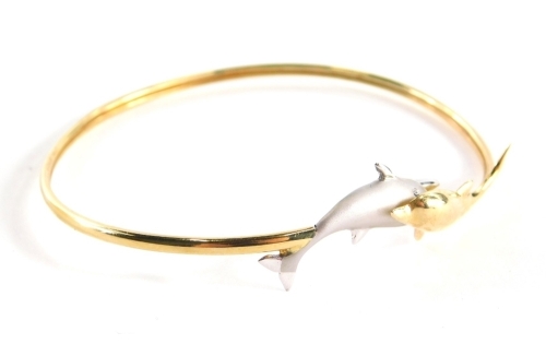 A bi-colour dolphin bangle, with a gold and silvered white gold clasp, on a thin bangle yellow metal stamped 585, 6cm diameter, 5.4g all in, boxed.