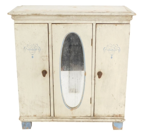 An early 20thC painted pine doll's triple wardrobe, with an out swept pediment over three doors, the central door inset with an oval mirror, raised on block feet, 43cm high, 38cm wide, 13cm deep.