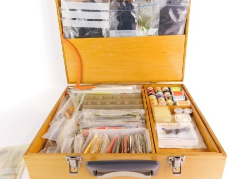 A fitted wooden travel case, with a selection of fly tying materials and accessories, to include tying silks, numerous hooks, seal fur, pheasant tippets, etc.