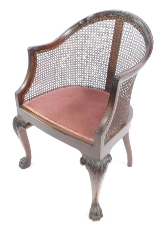 A Georgian style mahogany Bergere chair, early 20thC, with cane back and overstuffed seat, raised on leaf carved cabriole legs, and hairy paw feet.