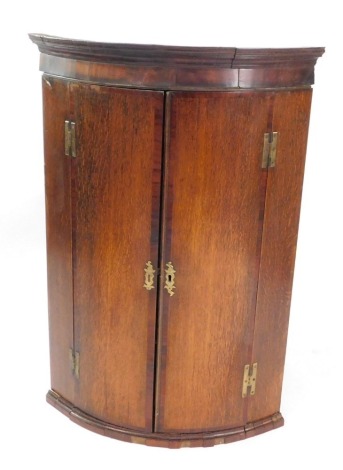 A George III oak and mahogany cross banded wall hanging corner cupboard, the out swept pediment over a pair of doors, opening to reveal three shelves, 107cm high, 73cm wide, 51cm deep.