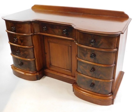 A Victorian mahogany inverted bow front desk, with one central drawer above a cupboard door, flanked by eight short drawers, raised on a plinth base, 80.5cm high, 137cm wide, 57cm deep.