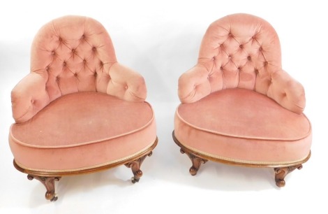 A pair of Victorian walnut conversation seats, upholstered in button back pink dralon, raised on carved scrolling legs, capped on ceramic castors.